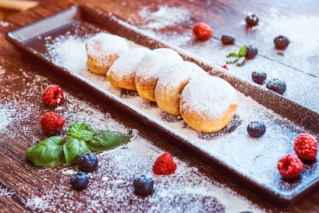 close up photo set donuts sprinkled with powdered sugar black long plate with raspberry bilberry mint scaled