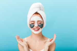 front view woman doing spa treatment with closed eyes studio shot charming girl with face mask standing blue background